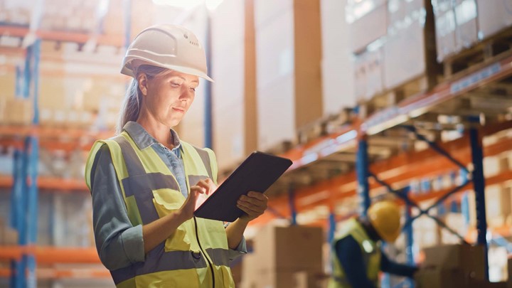 Woman in hard hat holding a tablet in a warehouse