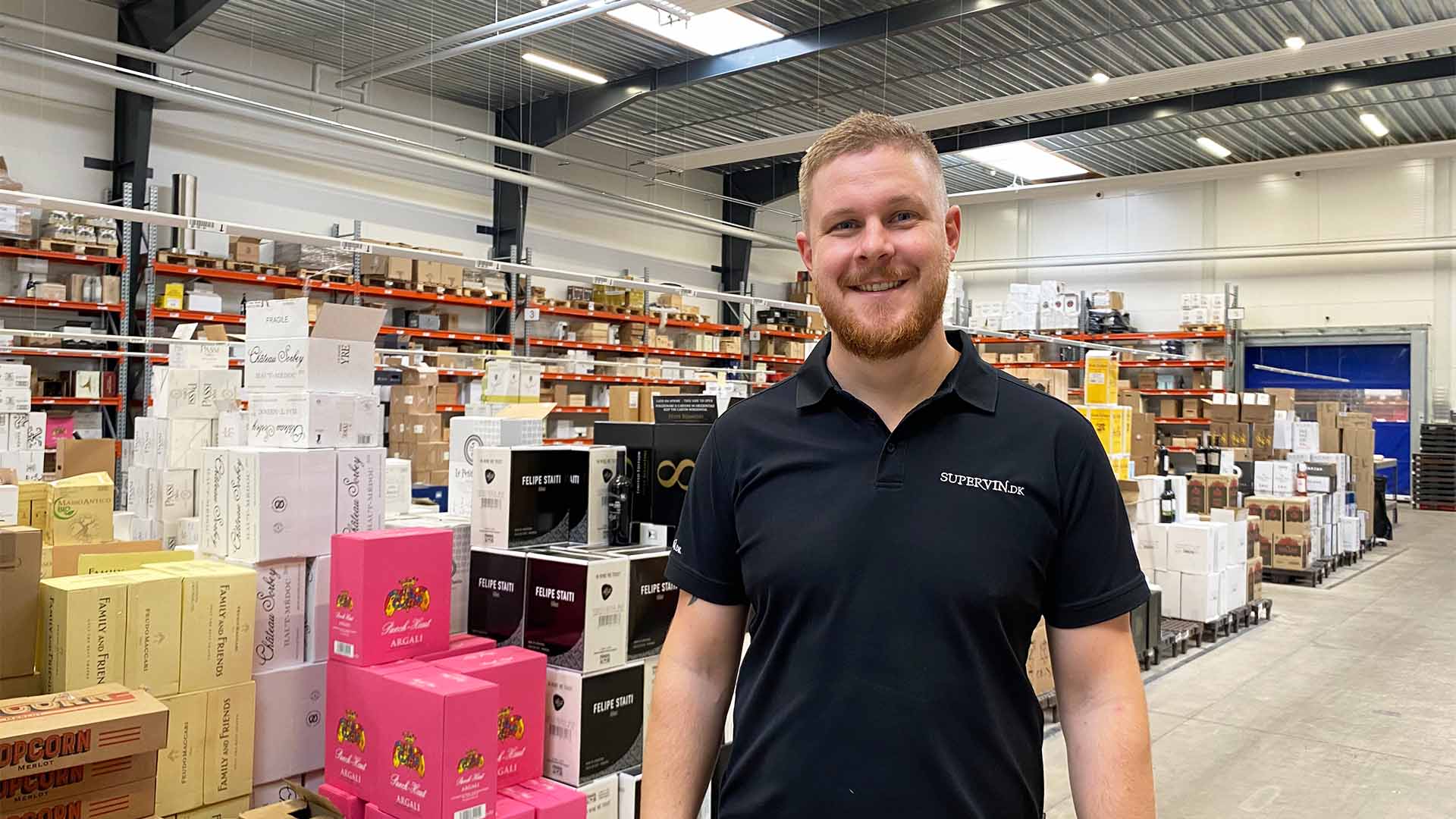 Logistikchefen hos Supervin står placeret foran et stort udvalg af forskellige vine. 