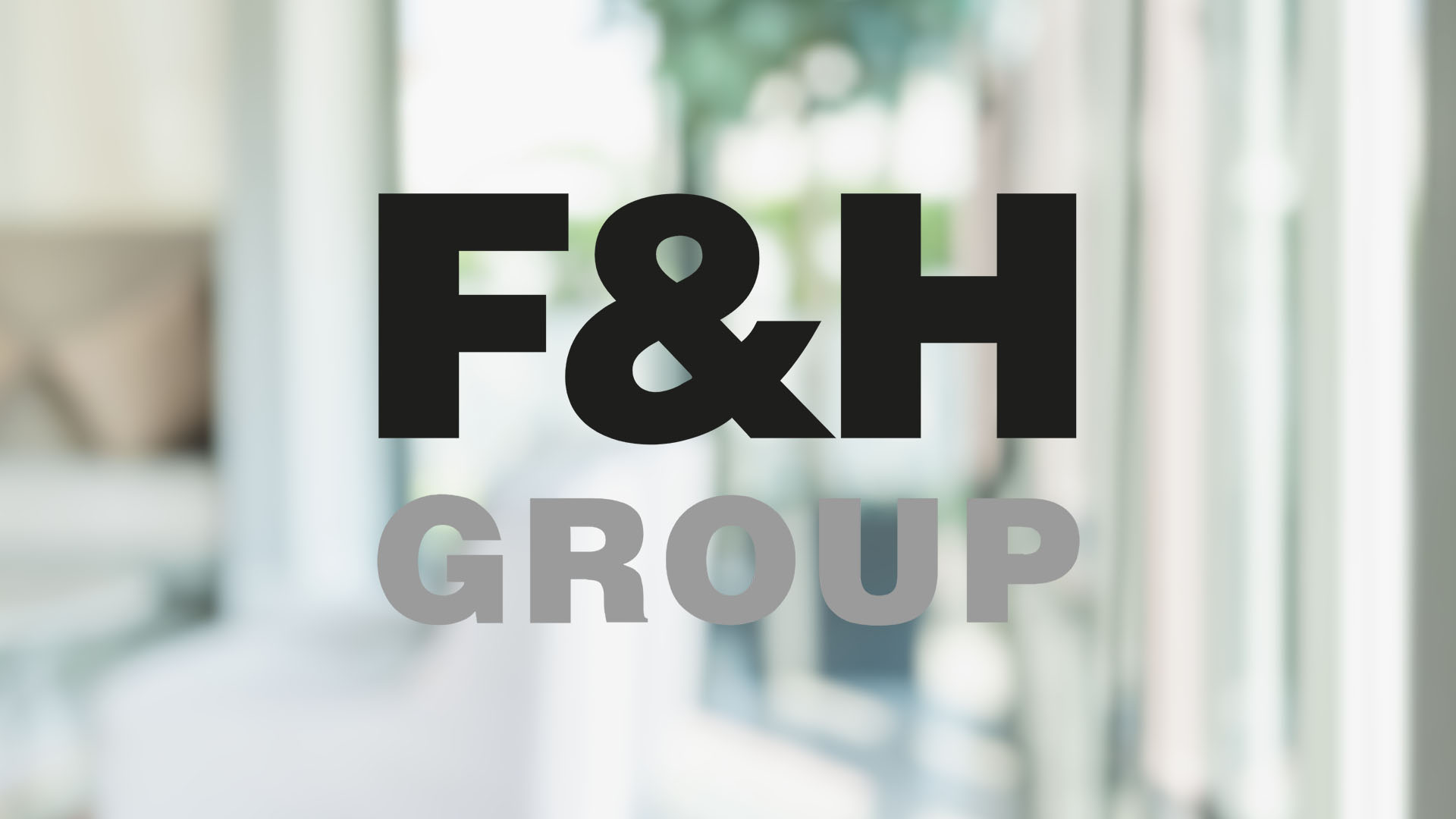Text "F&H GROUP" in bold black and gray letters centered in front of a blurred indoor setting, conveying professionalism and modernity.