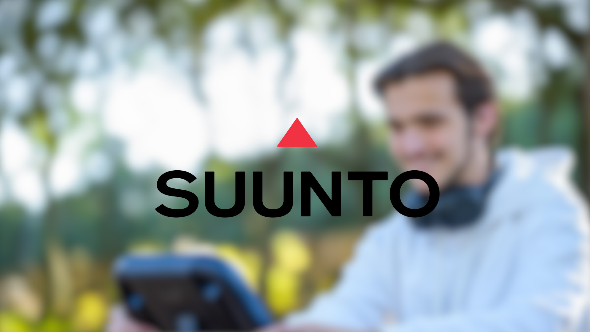 Blurry image of a person wearing headphones outdoors. Central focus on the Suunto logo with a red triangle, conveying a tech theme.