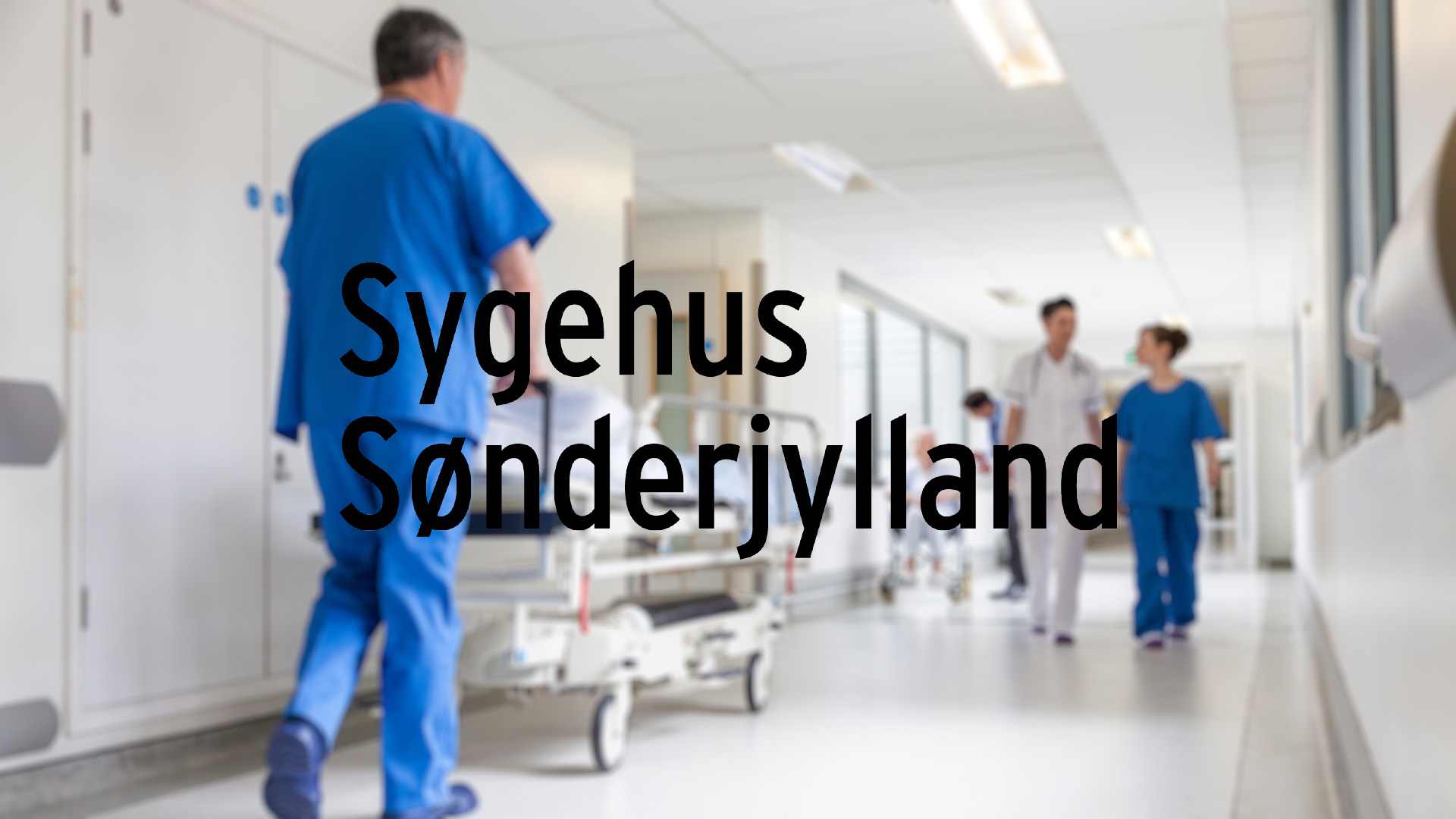 A hospital corridor with medical staff in blue and white uniforms walking, pushing a gurney. Logo for "Sygehus Sønderjylland" overlays the image. Calm, professional atmosphere.